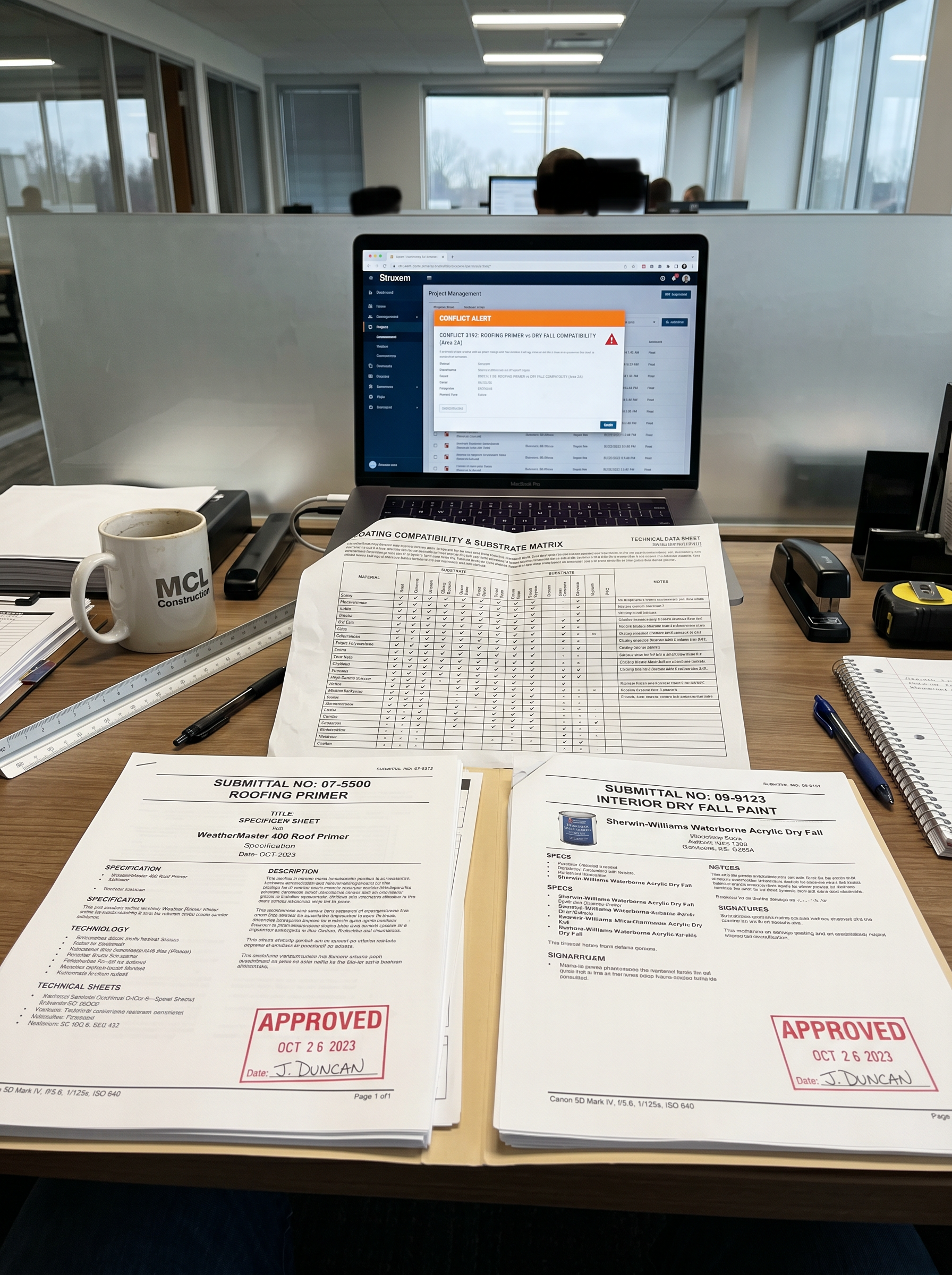 Two approved submittal packages side by side on a desk — a roofing primer and a dry fall topcoat — with a coating compatibility matrix partially unfolded between them and a Struxen conflict alert visible on a laptop screen in the background